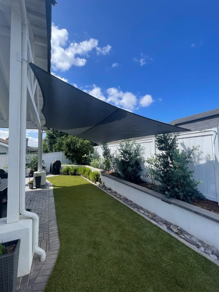 Grey shade sail over a green lawn and patio, against a blue sky with clouds.
