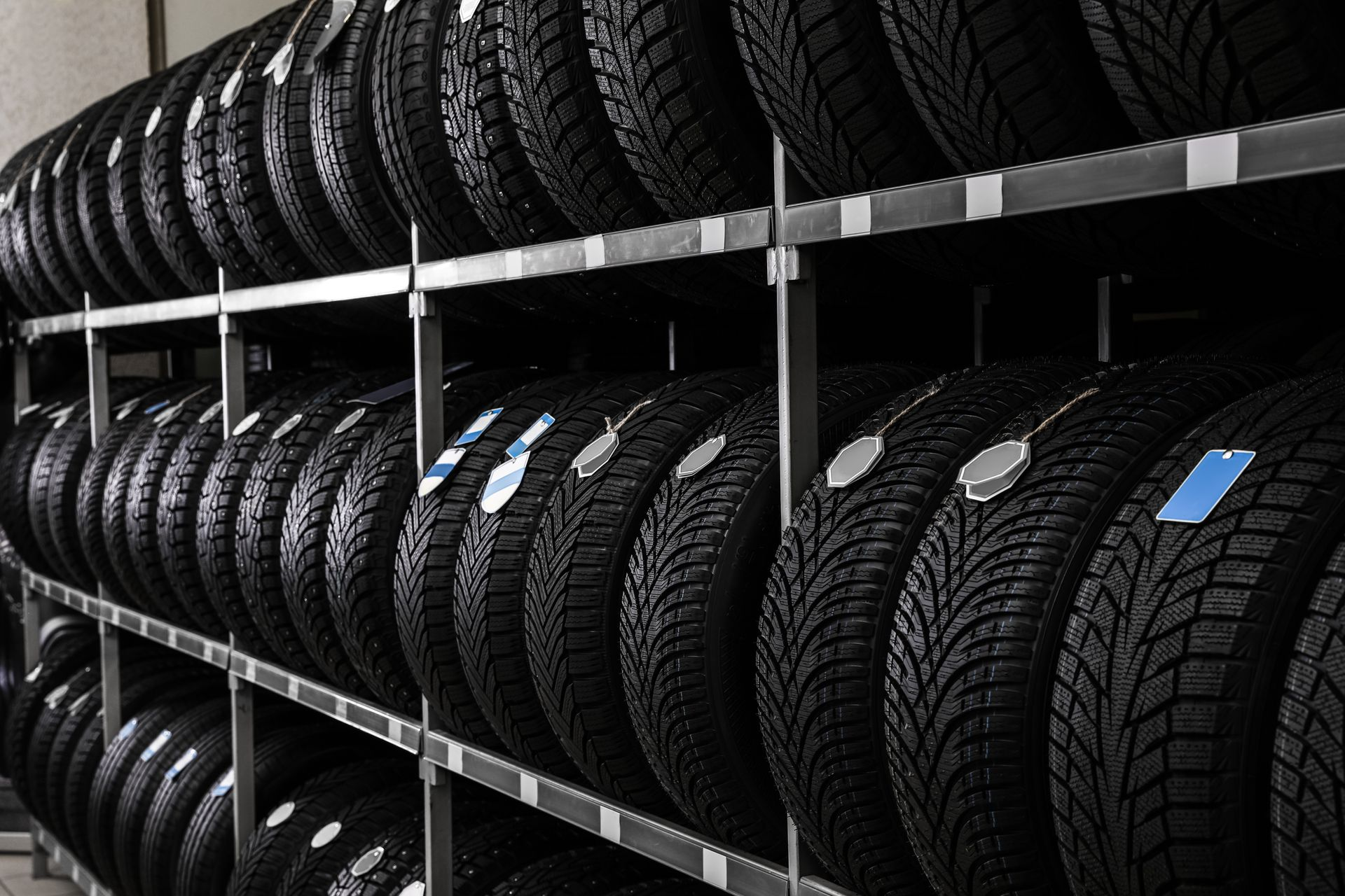 Tires stacked on metal shelves in a warehouse, some with tags attached | High Gear Auto Specialties