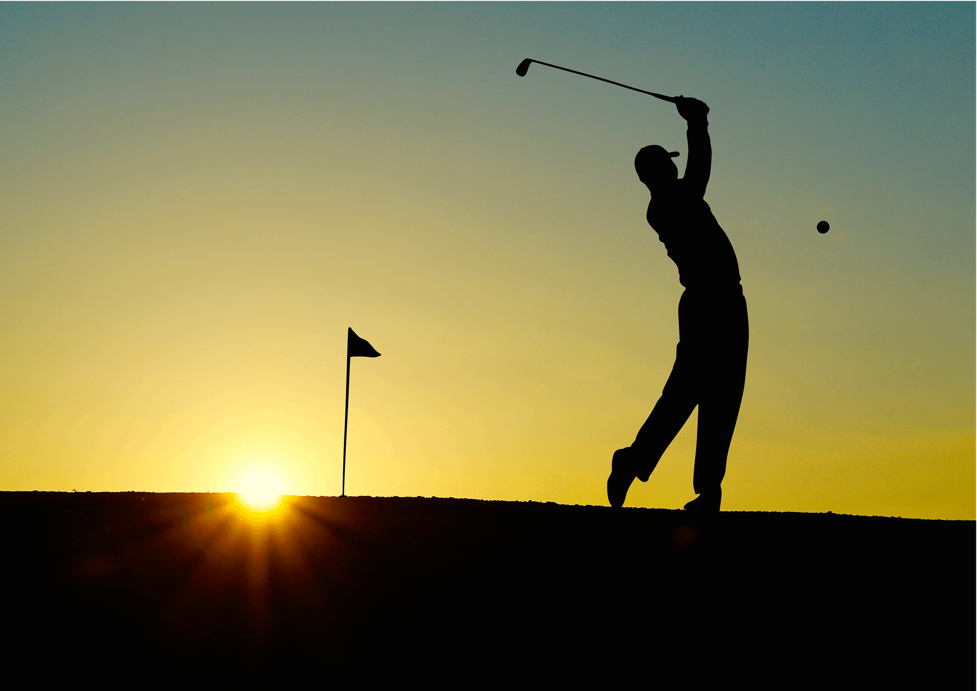 Silhouette of a golfer swinging club at sunset, ball in mid-air, flag in background.