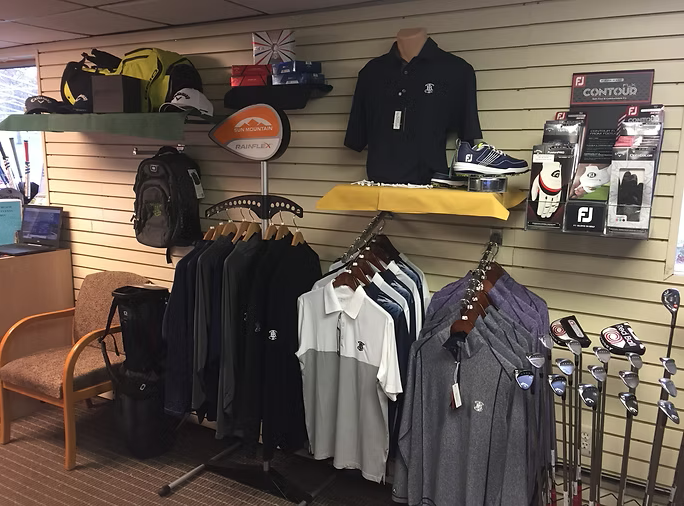 Golf apparel and equipment display in a store, including shirts, shoes, bags, and clubs.