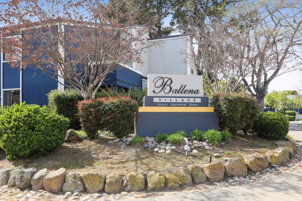 Sign for Ballena Villas apartment complex with bushes and trees in front.