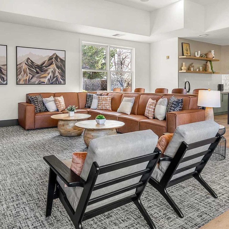 Living room with brown leather sectional, two gray chairs, coffee tables, and mountain art.