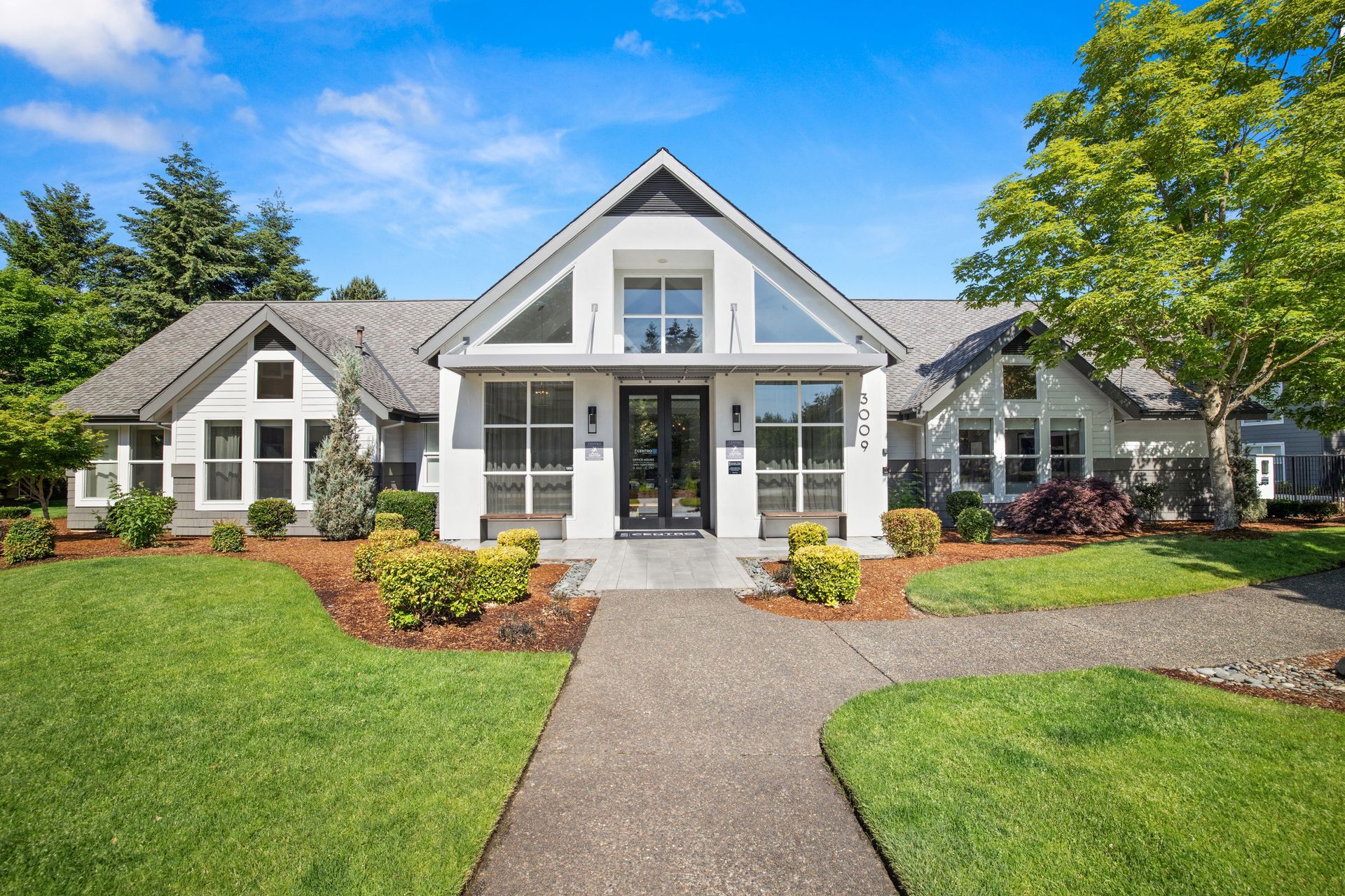 White farmhouse-style building with black trim, windows, and a pathway leading to the front door. Green lawn and blue sky.