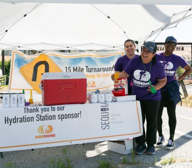 Three people smile at a hydration station. Banner says 