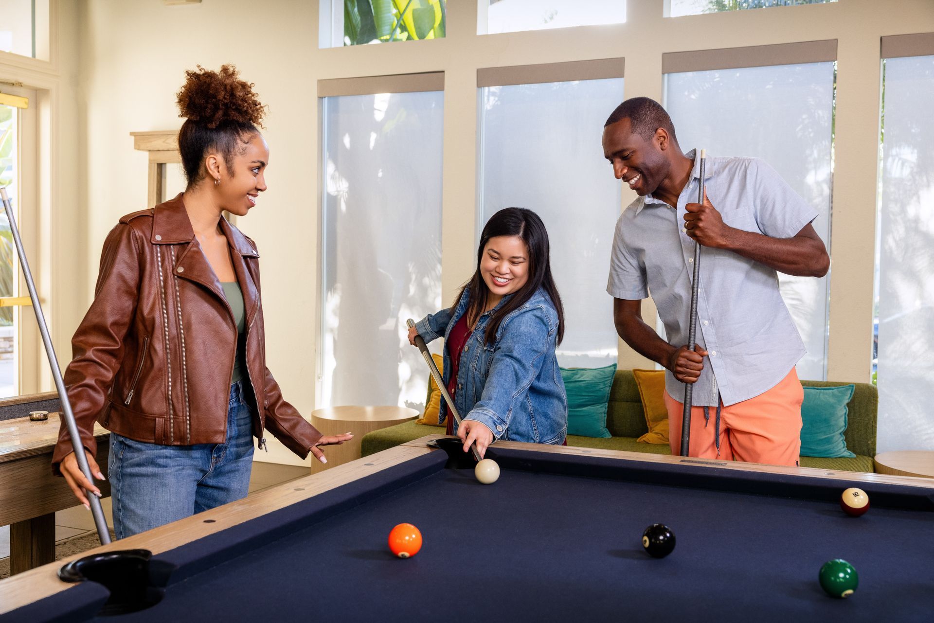 Family picnicking on a red-checkered blanket. A child laughs while holding a baguette. Others eat and smile.