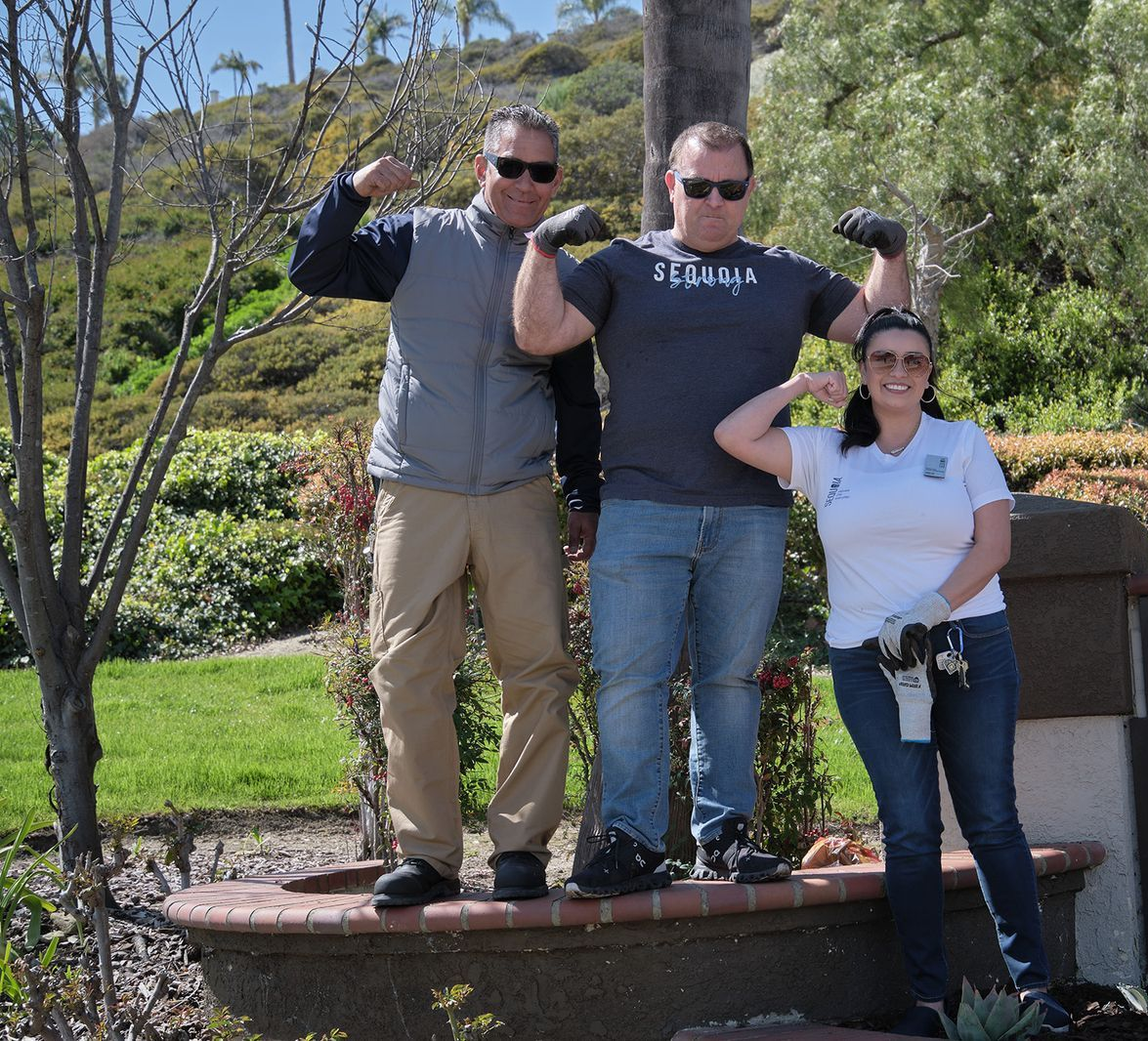 A man in a suit points to a computer screen while seated with two women at a desk.
