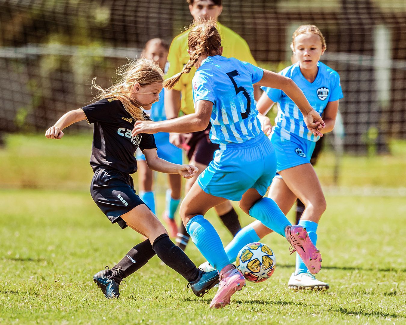 Soccer players, a black-clad player and blue-clad players, compete on a grassy field.