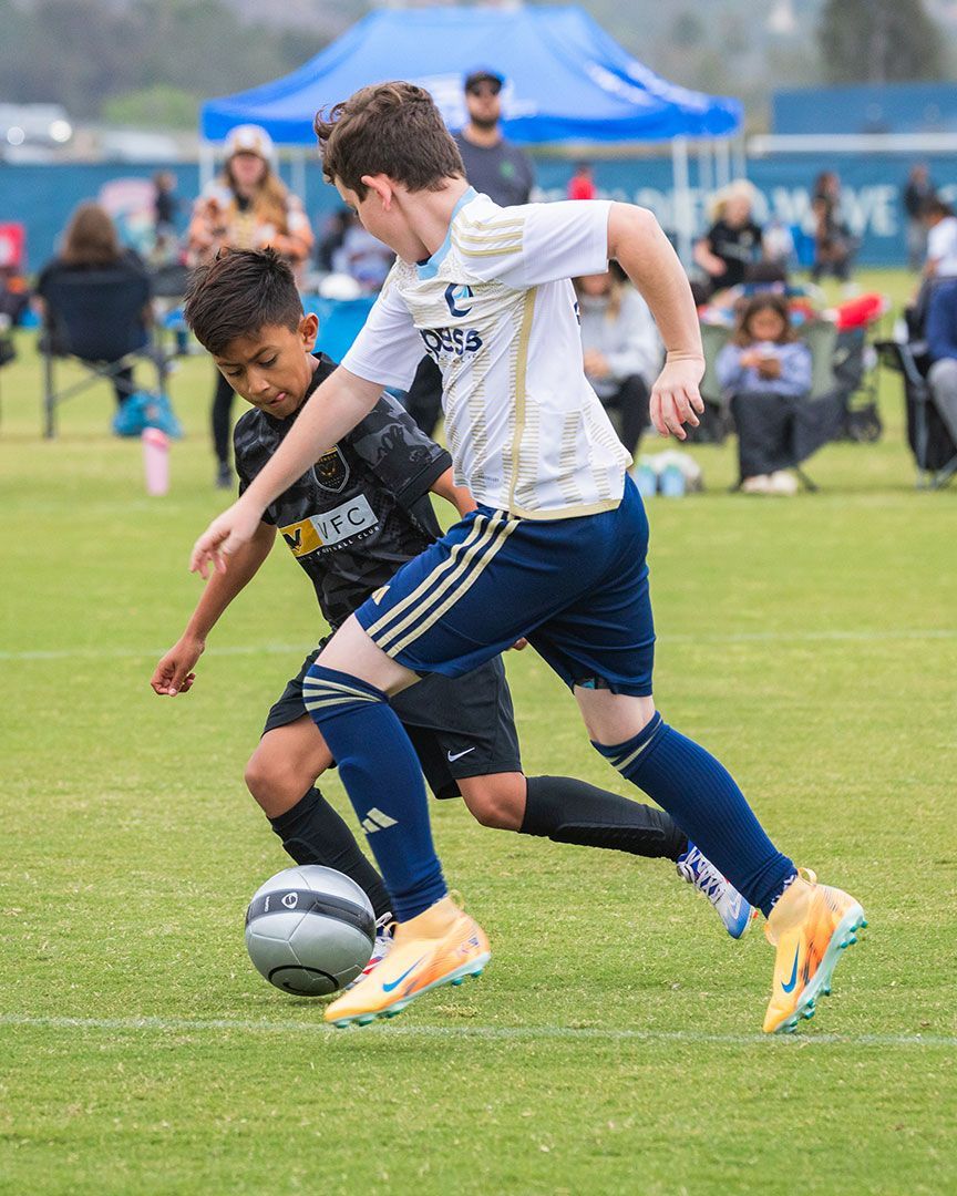 Two soccer players in black and white jerseys contest the ball on a grassy field.