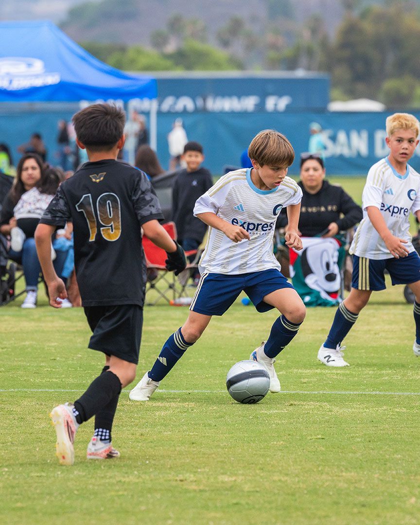 Youth soccer players dribble and challenge for the ball on a grassy field during a match