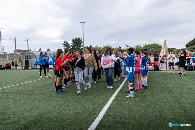 Soccer teams shaking hands on a green field after a match, in front of spectators.