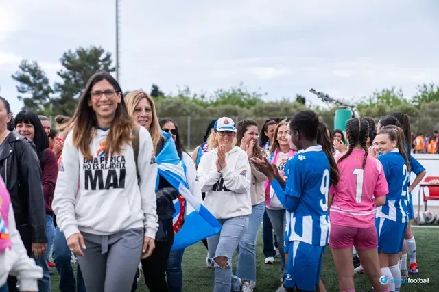 Group of women and girls, smiling, clapping, on a soccer field, celebrating.