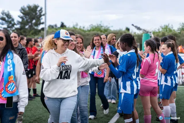 Fans high-five young soccer players on a field. Some wear blue and pink jerseys, others have scarves.