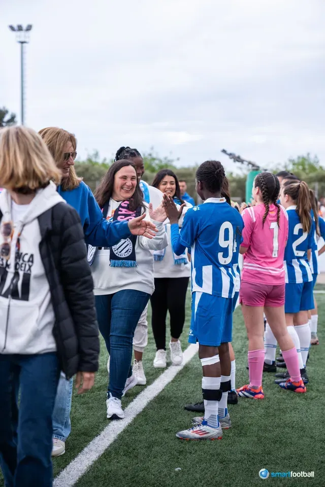 Soccer players in blue and pink uniforms give high fives on the field. People watch, cheering.