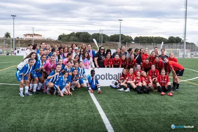 Group of young soccer players in blue and red uniforms, smiling on a green field after a game.
