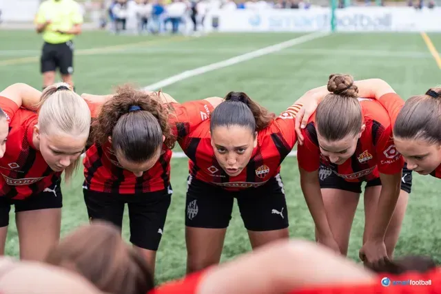 Soccer team in red and black jerseys huddles together on a green field, focused and ready to play.