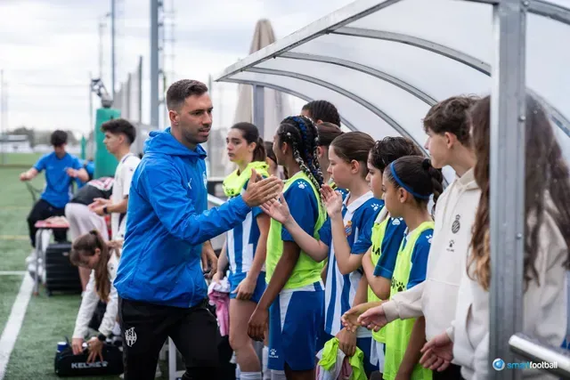 Soccer coach high-fives team wearing blue jerseys on the sidelines.