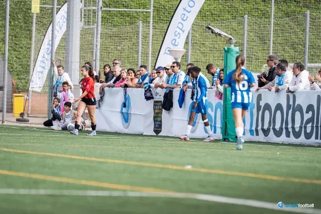 Soccer players on field with spectators behind barrier.