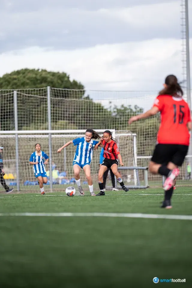 Soccer players in red and yellow uniforms on a green field, competing for the ball.