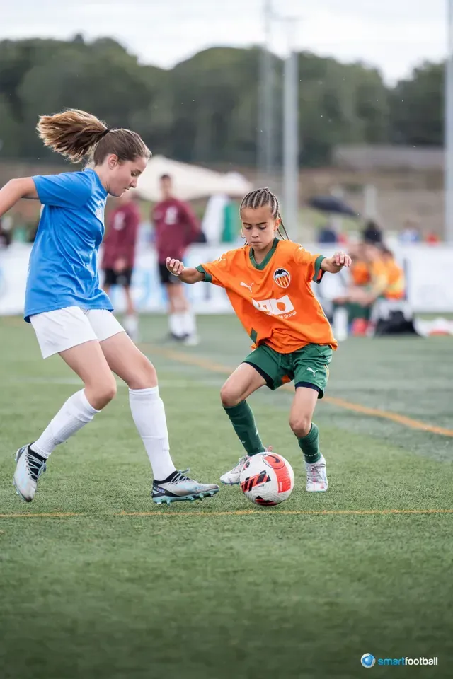 Soccer players in blue and orange jerseys on a green field, one dribbling the ball.