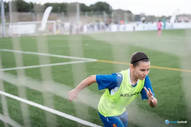 Soccer player in blue running on a green field, wearing a yellow bib.