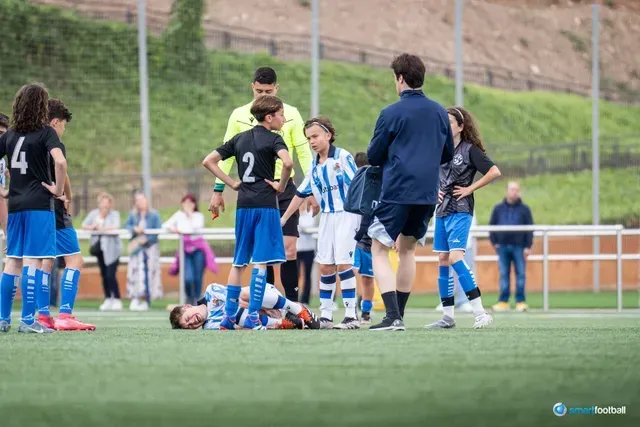 Youth soccer game: Player injured on field, surrounded by teammates, referee, and coach.