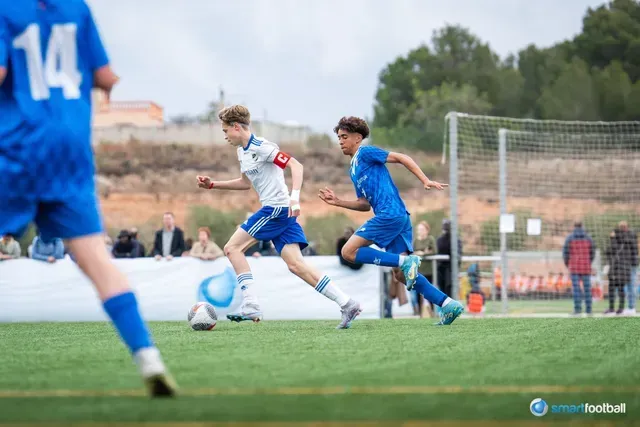 Two young soccer players in blue and white uniforms compete on a green field during a match.