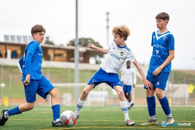 Youth soccer players in action on a green field. One in white kicks the ball as two in blue watch.