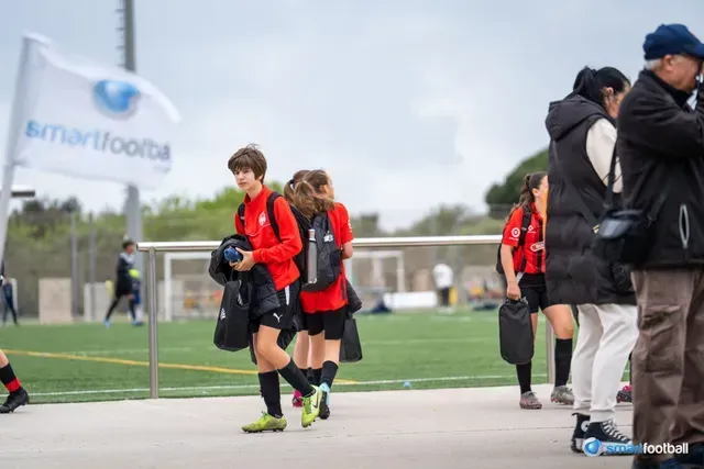 Soccer players in red jerseys walking off the field after a game, next to spectators.