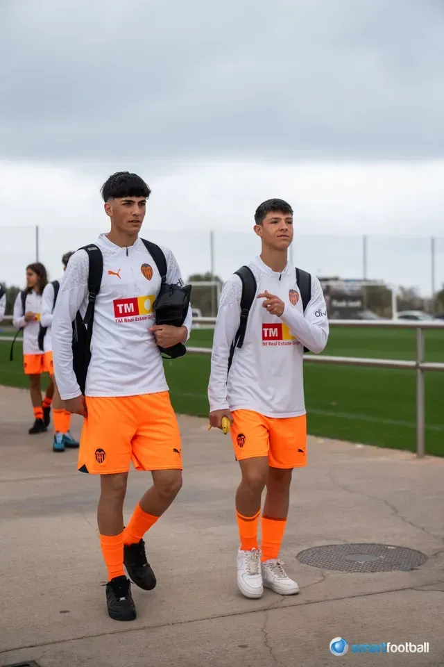Two soccer players in white and orange team gear, walking outdoors.