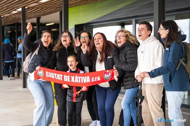 Group of fans cheer, holding a red & white scarf; outdoors, excited expressions.