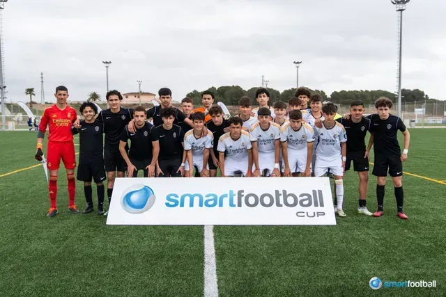 Soccer team posing on a field for the Smartfootball Cup; players in various black & white kits, goalie in red.