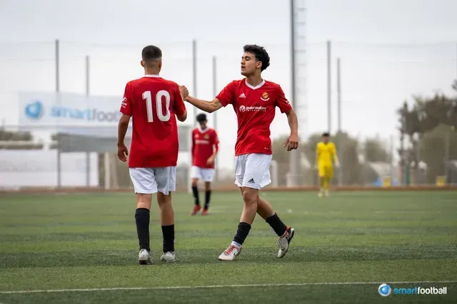 Soccer players in red and white uniforms celebrate on a field. Player with 