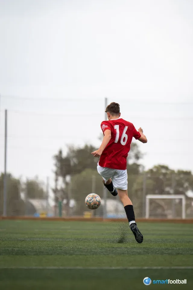 Soccer player in red jersey (#16) kicking ball on green field.