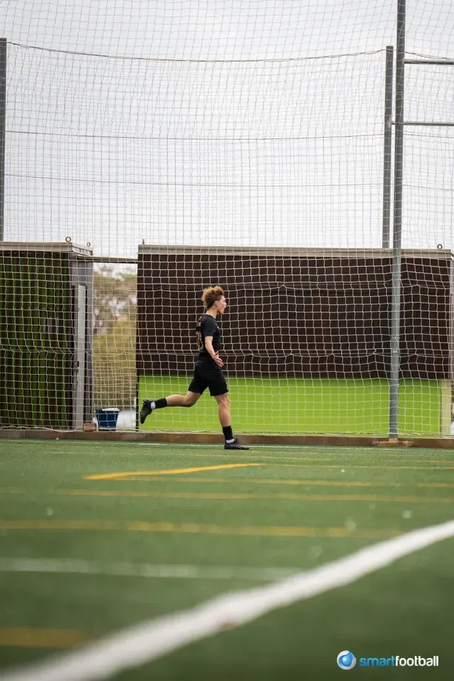 A person in black athletic wear running on a green turf soccer field.
