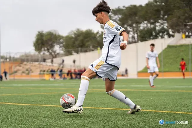 Soccer player in white uniform dribbling a ball on a green field.