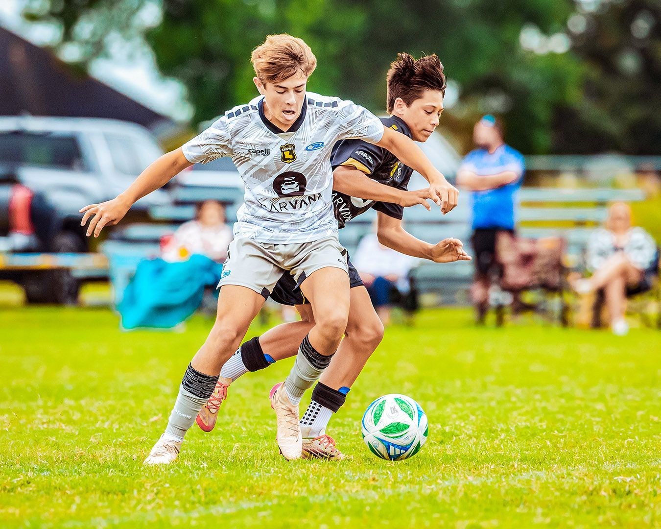 Two young soccer players in action on a green field, one in white and the other in black, vying for the ball.