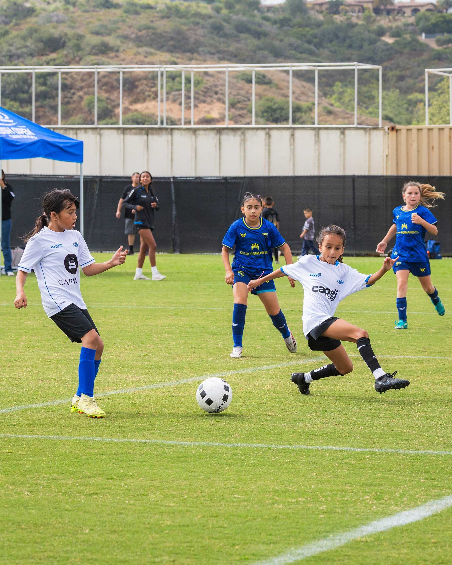 Youth soccer game with players in blue and white chasing a ball on a grassy field