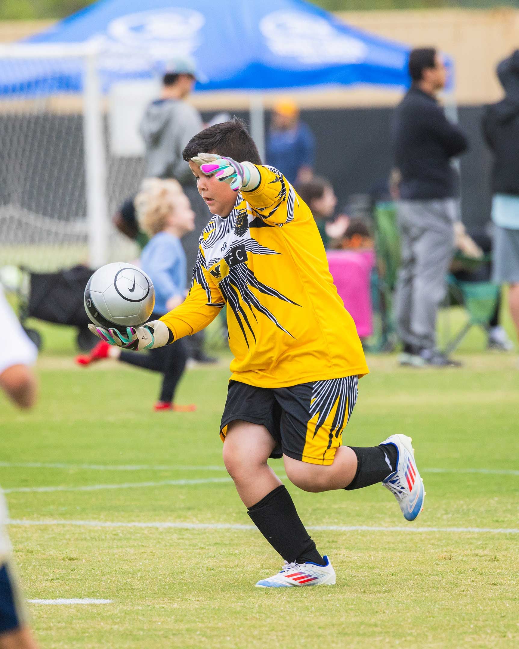 Soccer player in yellow jersey kicking a ball on a grassy field during a match