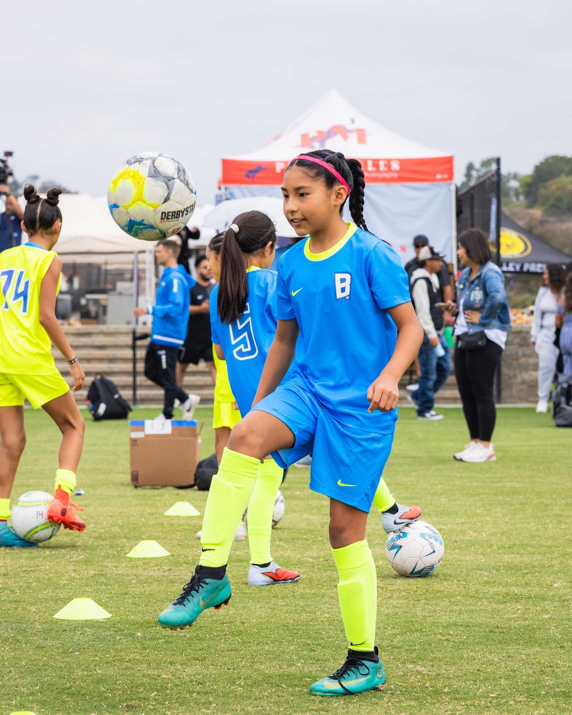 Soccer players in blue and yellow practice dribbling on a grassy field with cones and balls.