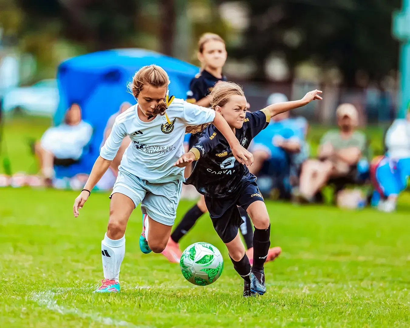 Two young girls playing soccer, competing for the ball on a green field.