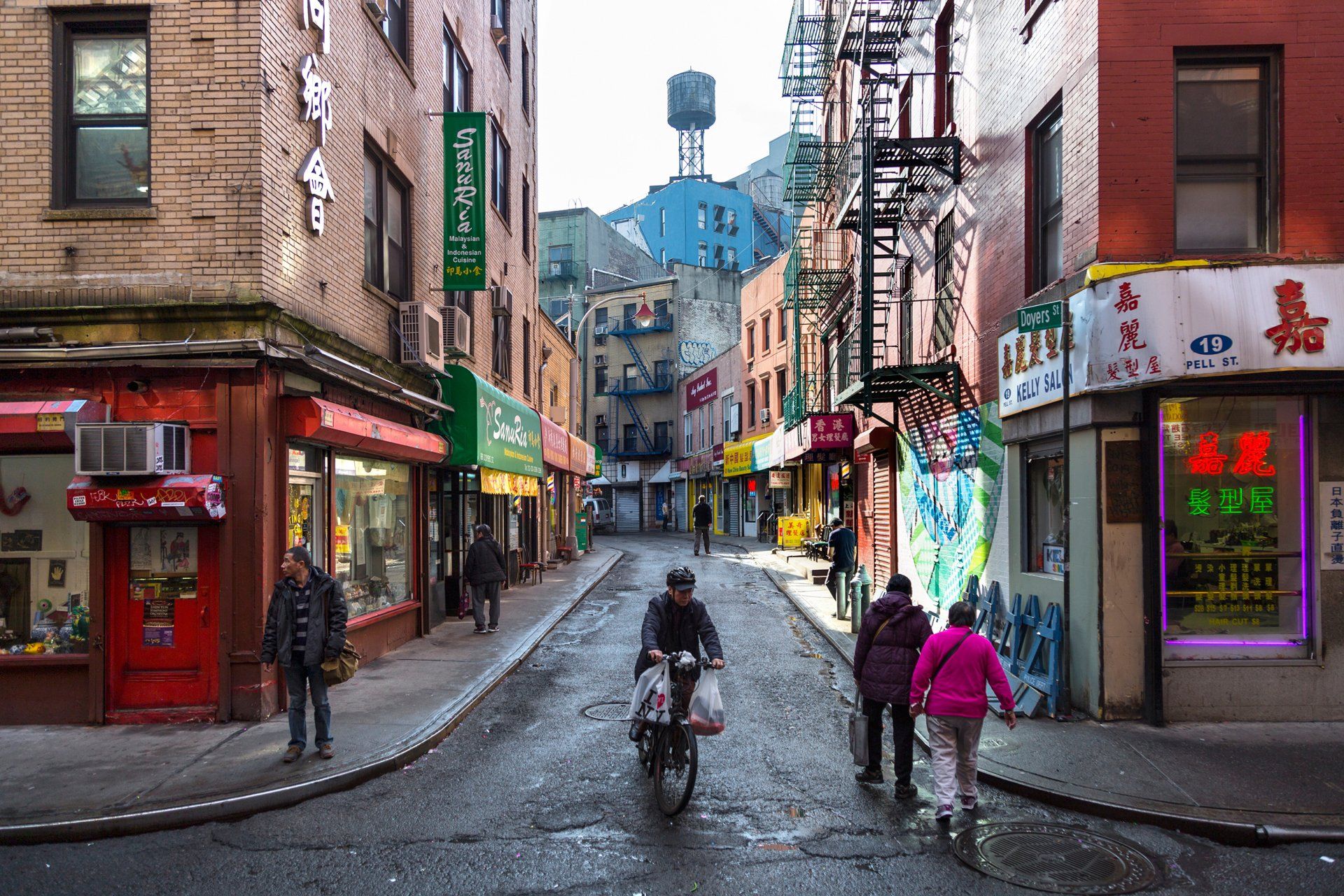 A man is riding a bike down a narrow street in a city