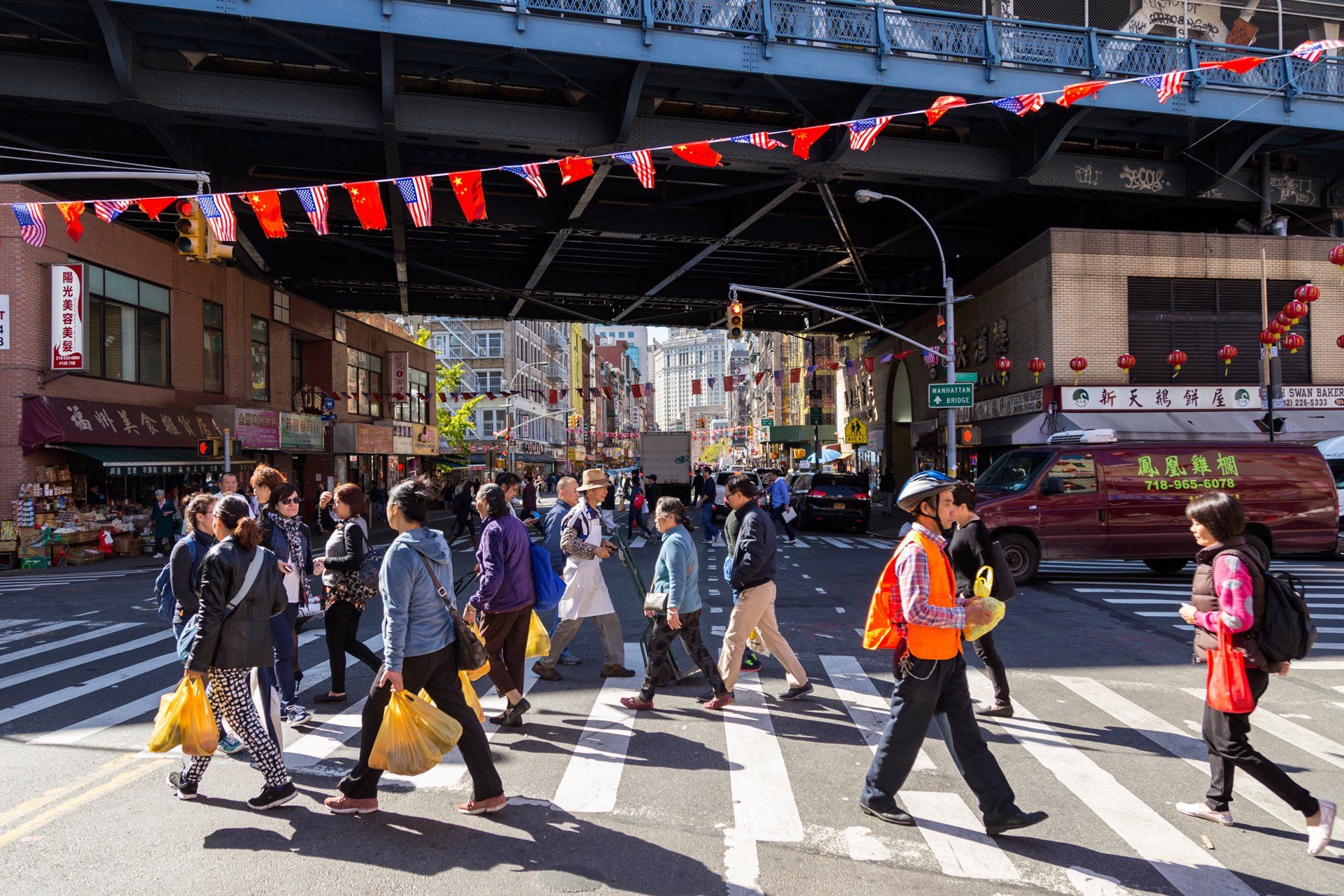 A group of people are crossing a street under a bridge.