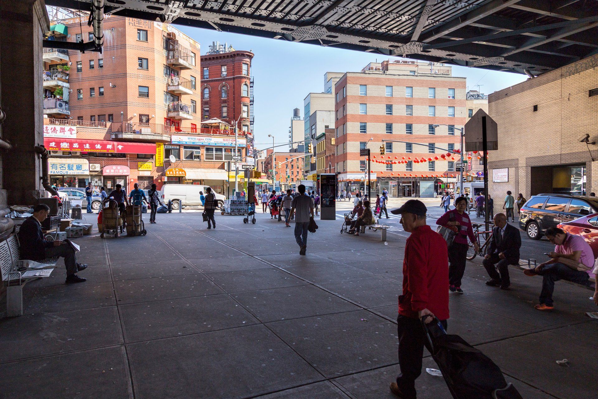 A man in a red shirt is walking under a bridge in a city