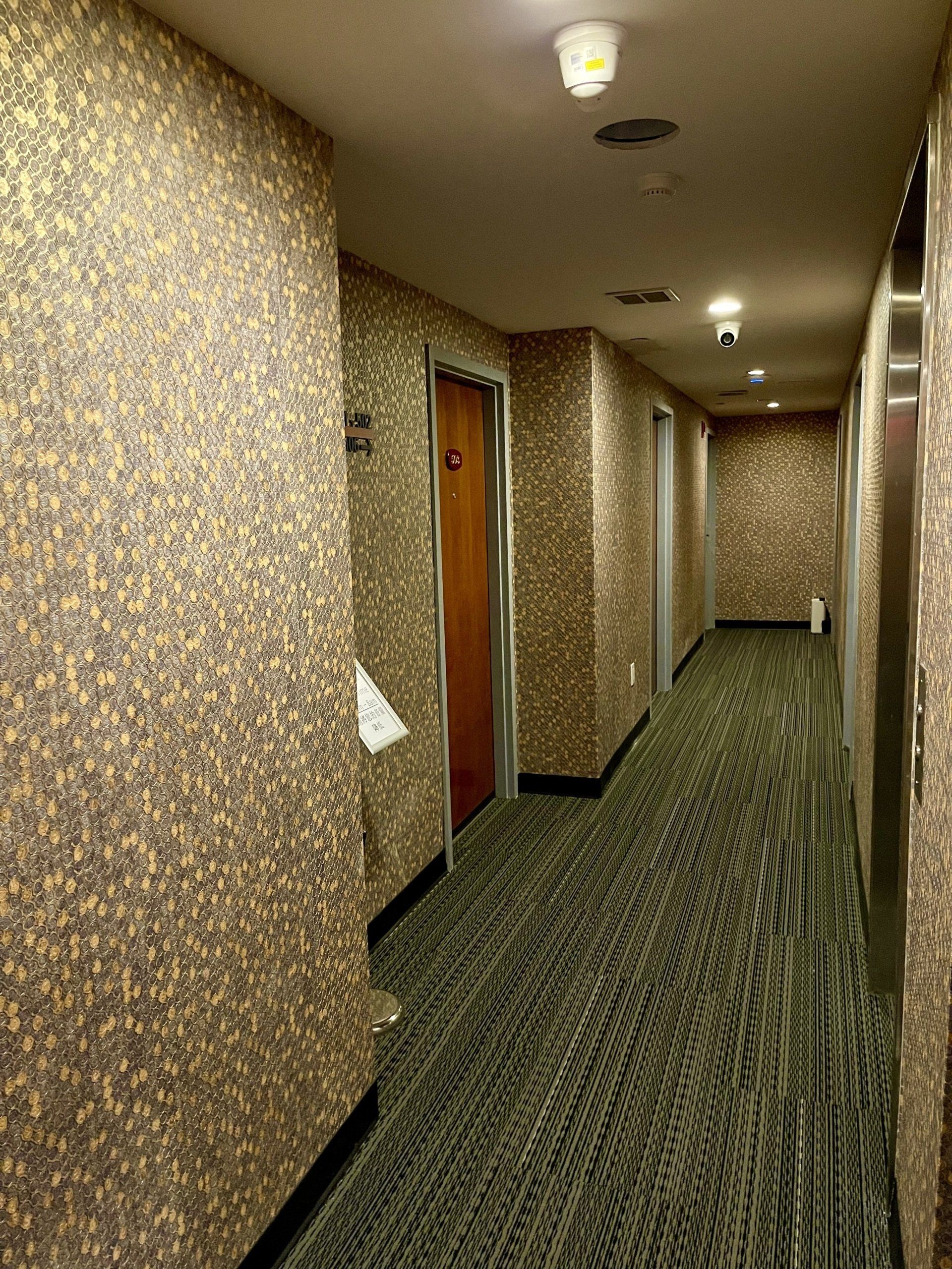 A long hallway in a hotel with a green carpet and gold walls.