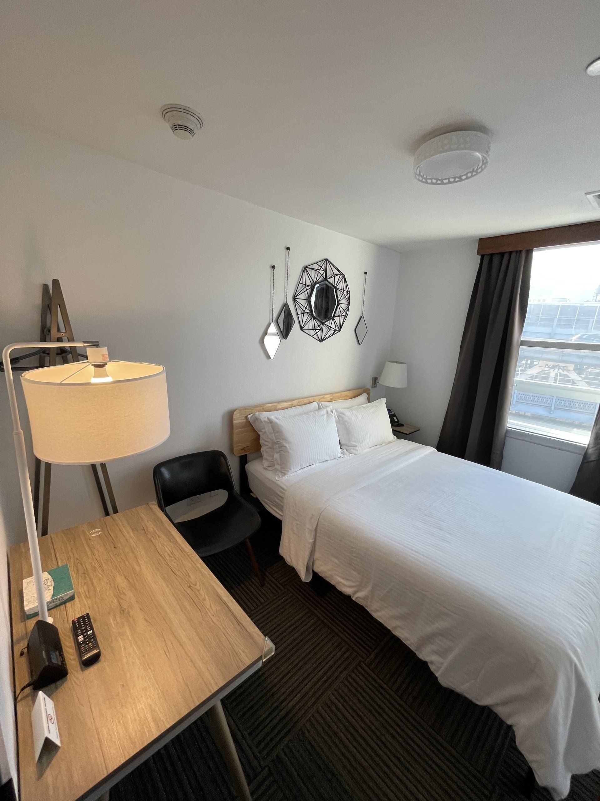 A hotel room with a bed a desk and a lamp