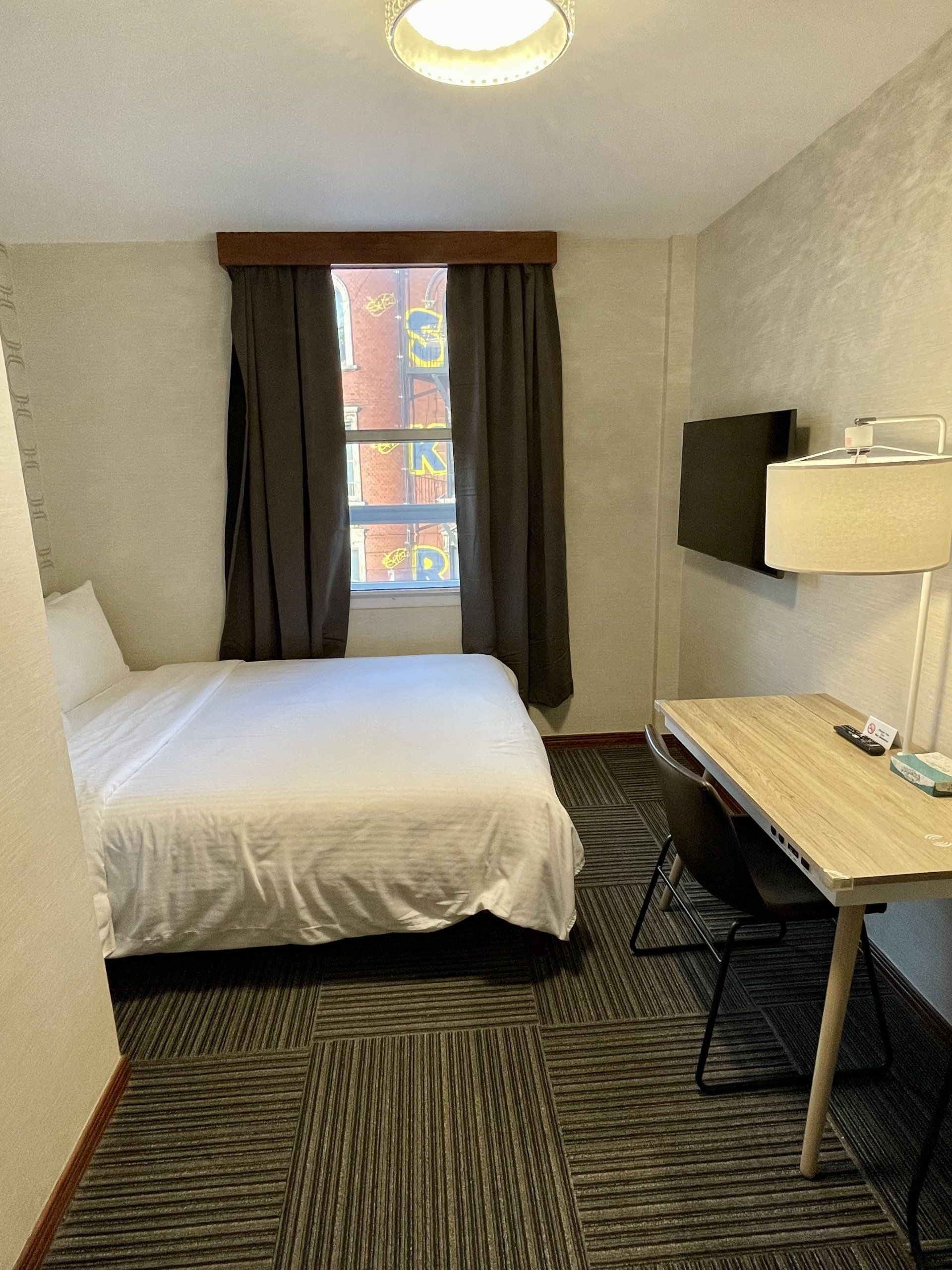 A hotel room with a bed , desk , chair and television.