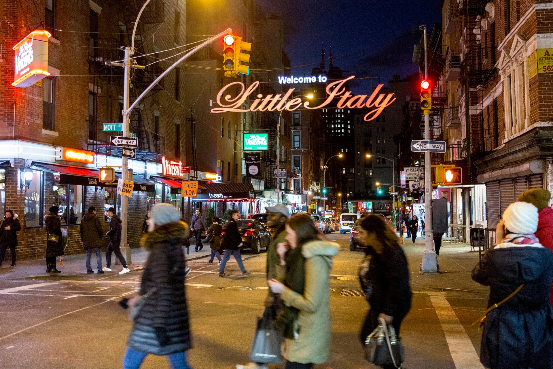 A group of people are crossing a street in front of a sign that says little italy