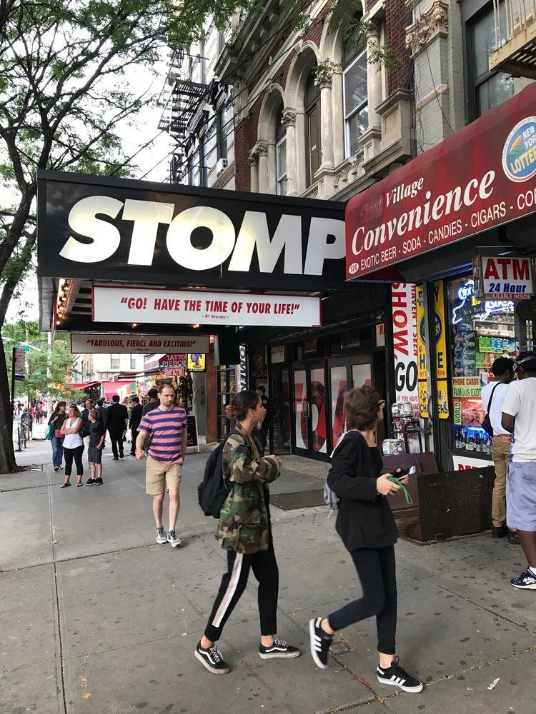 A group of people are walking down a sidewalk in front of a stomp convenience store.