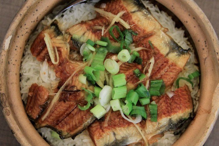 A bowl of food with rice , meat and green onions on a table.