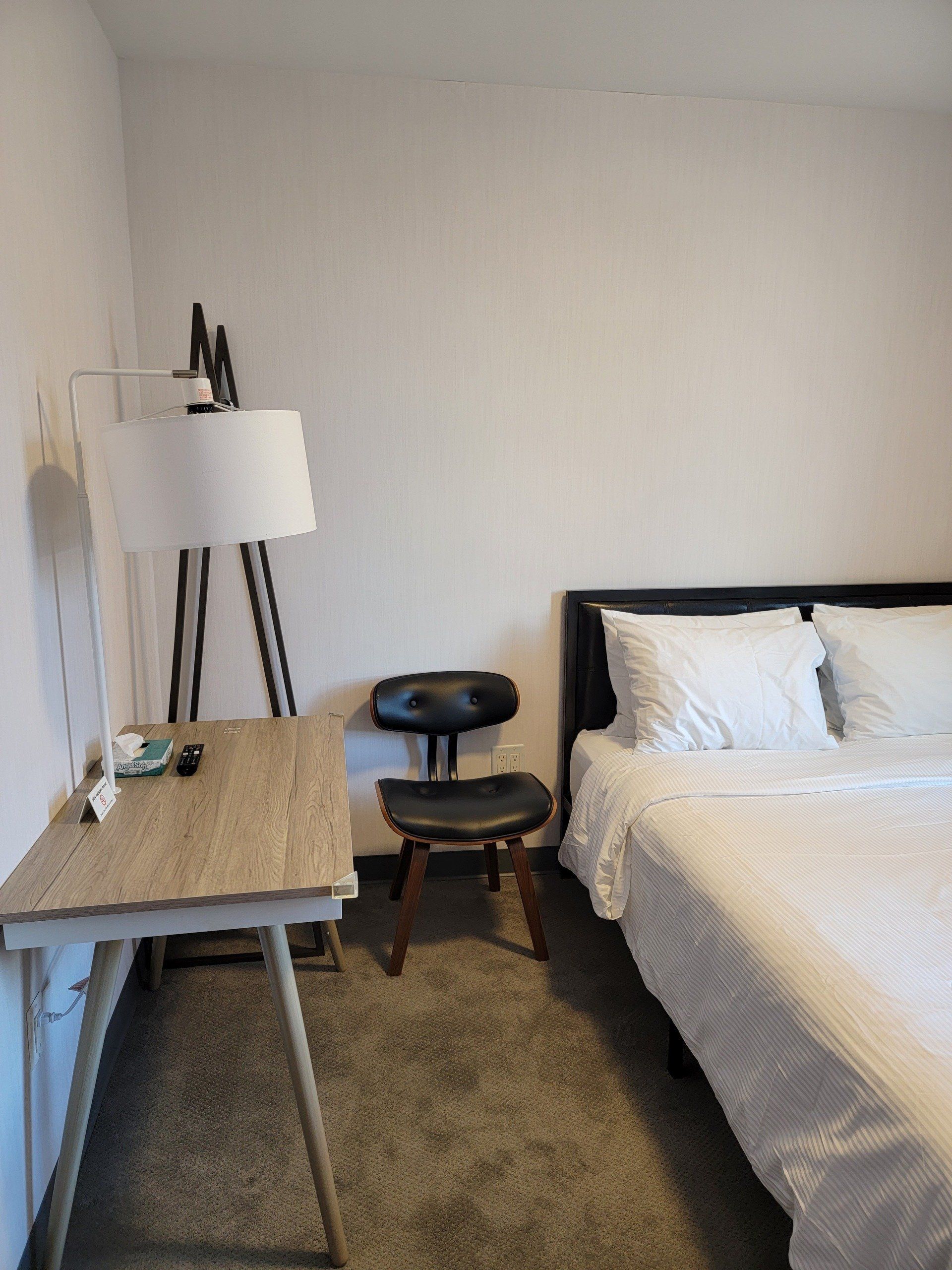 A bedroom with a bed , desk , chair and lamp.